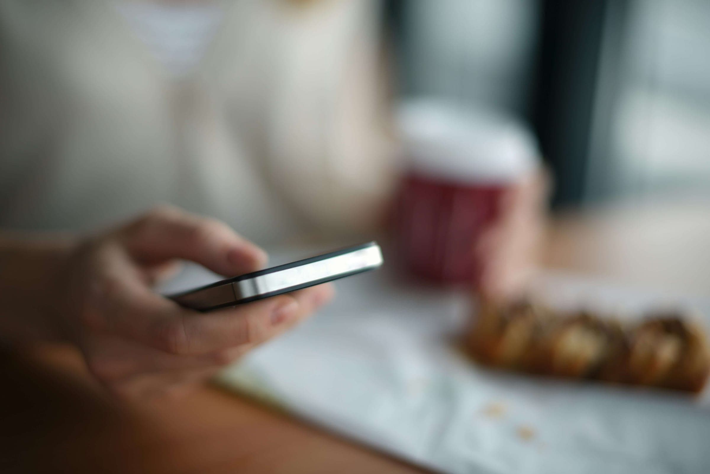 A hand holding a phone, mid-inquiry, with a coffee in soft focus.